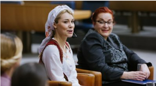 two women sitting next to each other, smiling and speaking