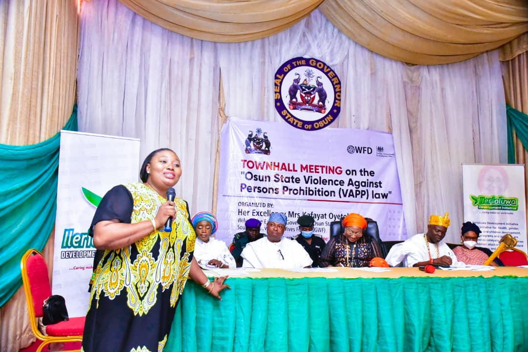 A woman speaking into a microphone at a town hall meeting in Nigeria