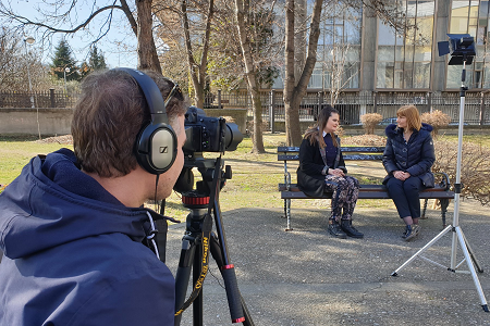 A person filming two people sitting on a bench