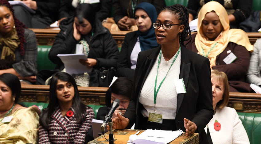 A woman speaking in the midst of other sitting women in the UK Parliament