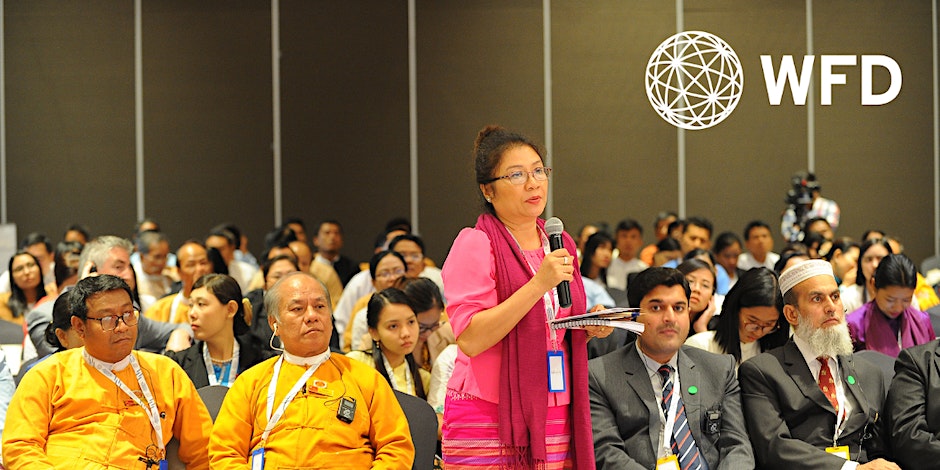 woman standing with microphone amongst a group of people sitting down