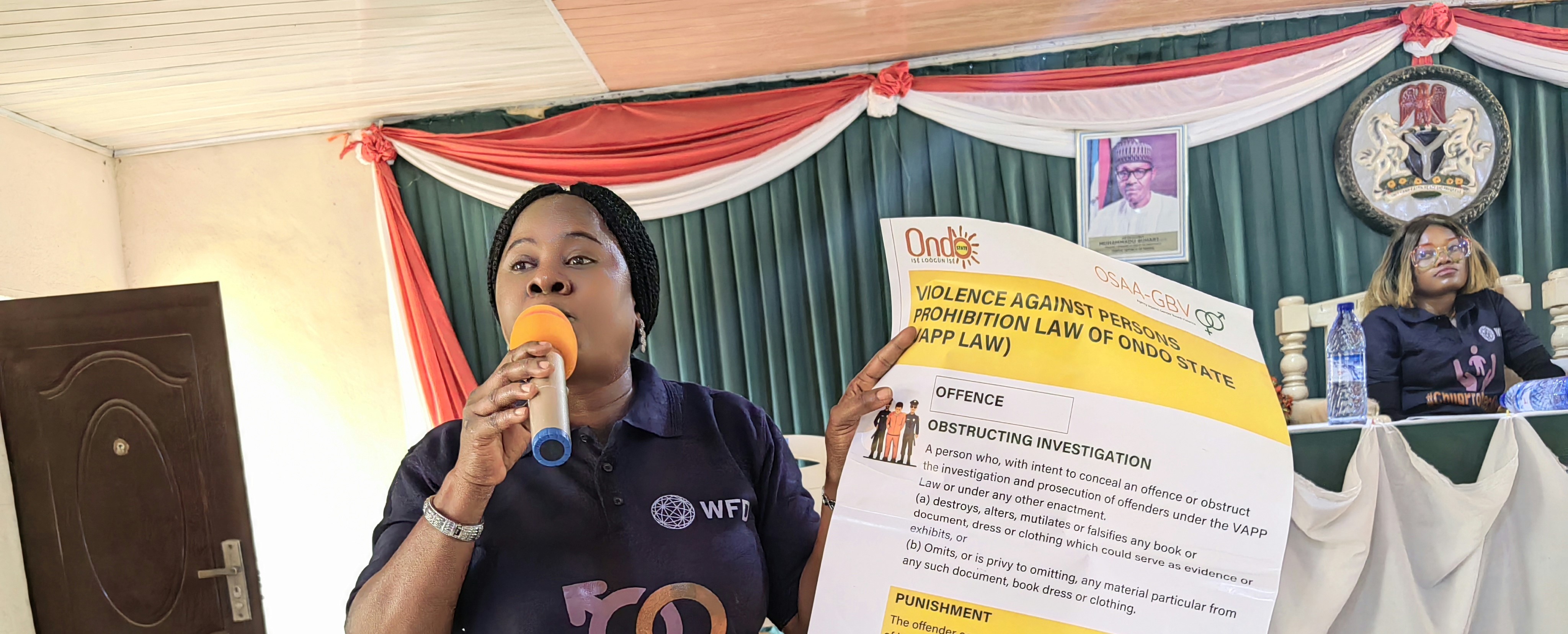 A woman holding an advocacy paper while speaking on a microphone