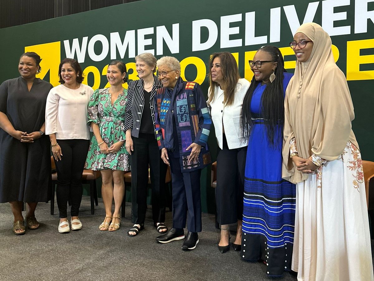 A line of woman in front of a billboard that says women deliver conference