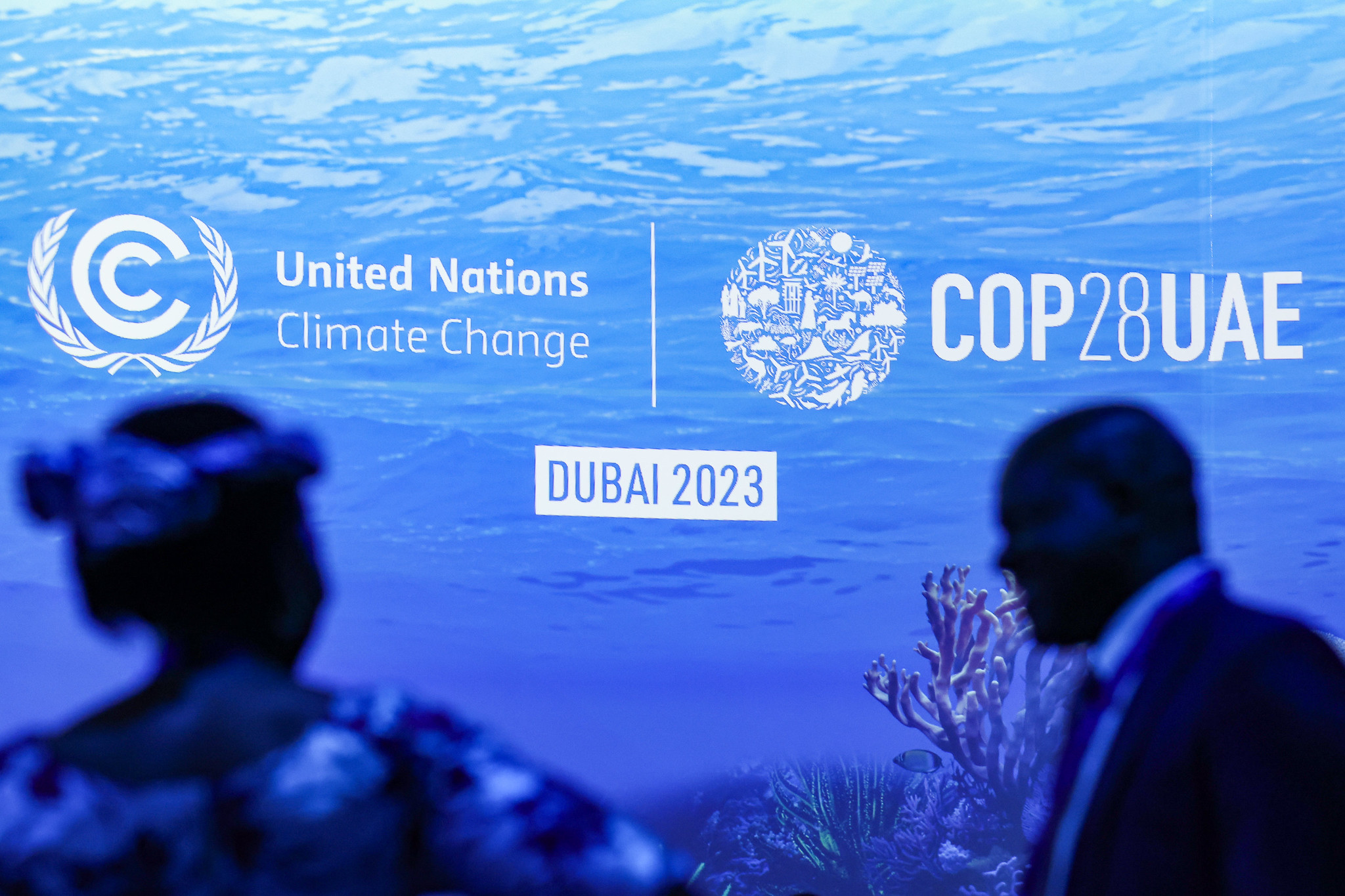 The COP28 logo on a blue sea background with the figures of two people in front