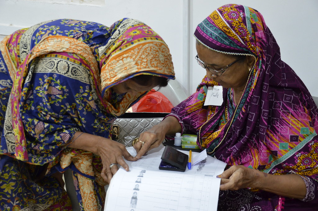 A polling official confirms a voter's identity during the Pakistani general elections in July 2018. The two women are wearing colourful clothing and headscarves