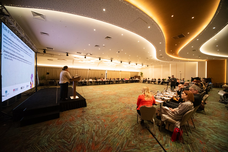 A group of people sit around the edges of a large conference room