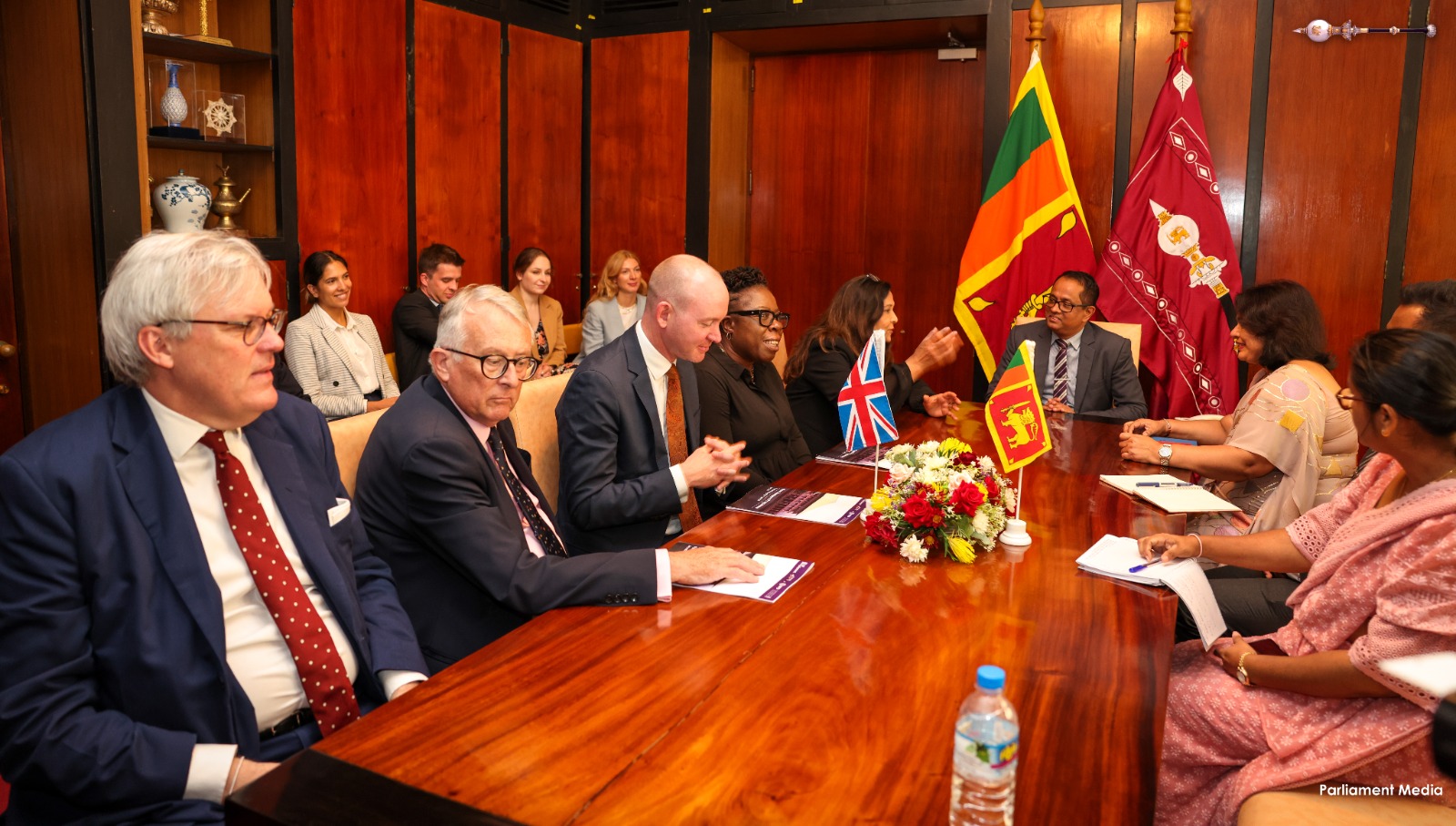 Parliamentary delegation consisting of a group of men and women are in discussion. Sri Lanka and UK flags can be seen in the photo. 