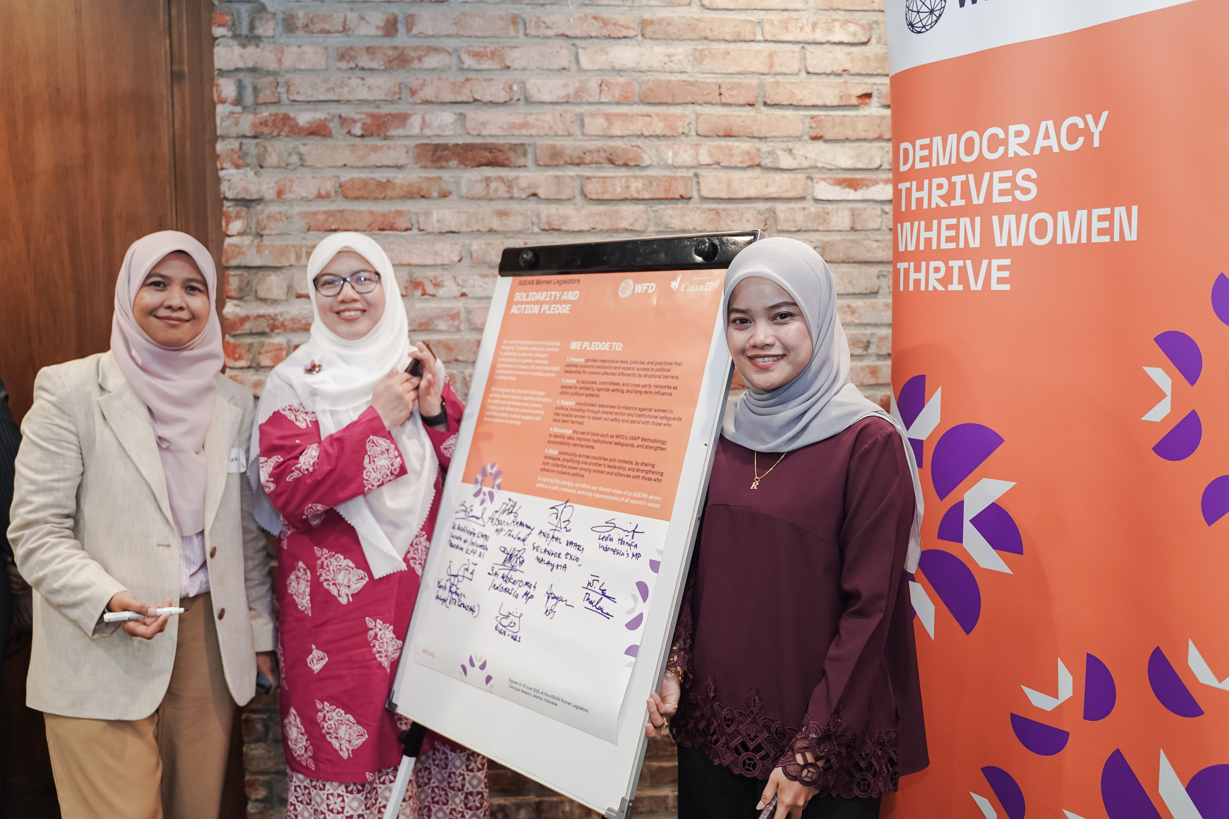 Three women standing next to a white board that shows signatures.