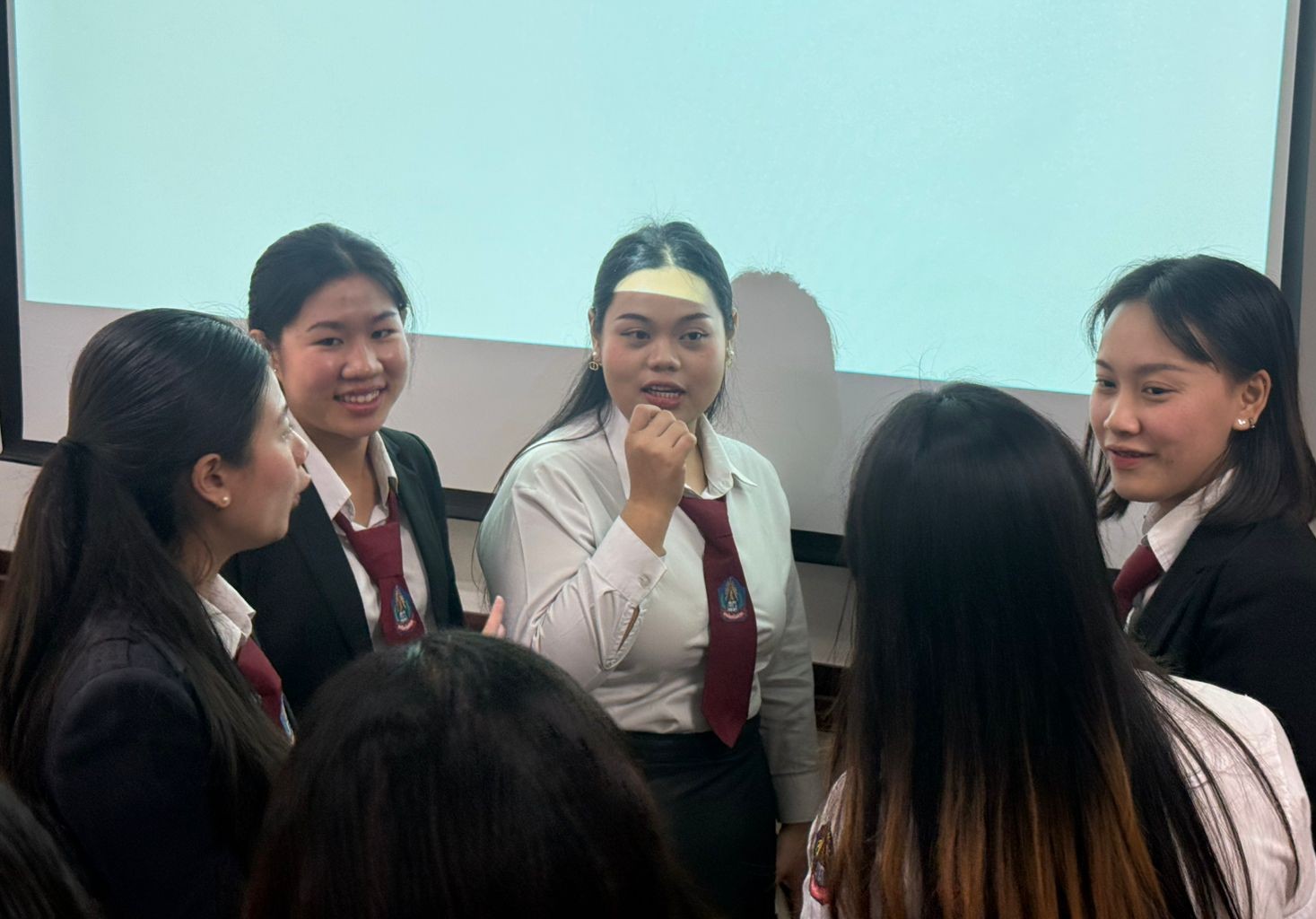 A group of young female students in uniform stand in a circle talking. 