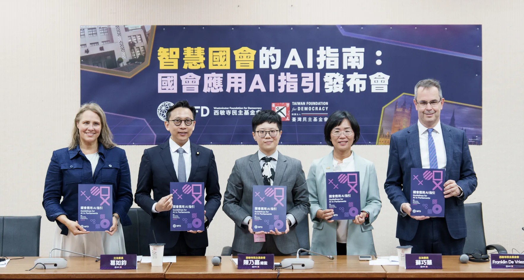 Three women and two men stand in front a table. Each of them holds a book in front of them. 