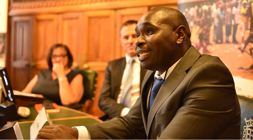 A man speaking while sitting with two others on his periphery