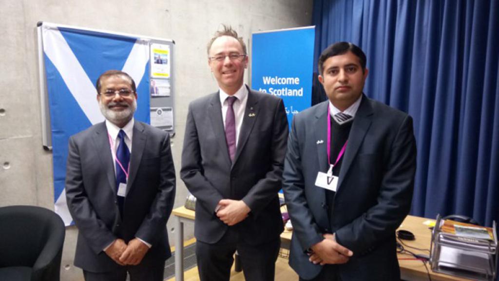 Three men smiling at the camera standing in front of the Scottish flag