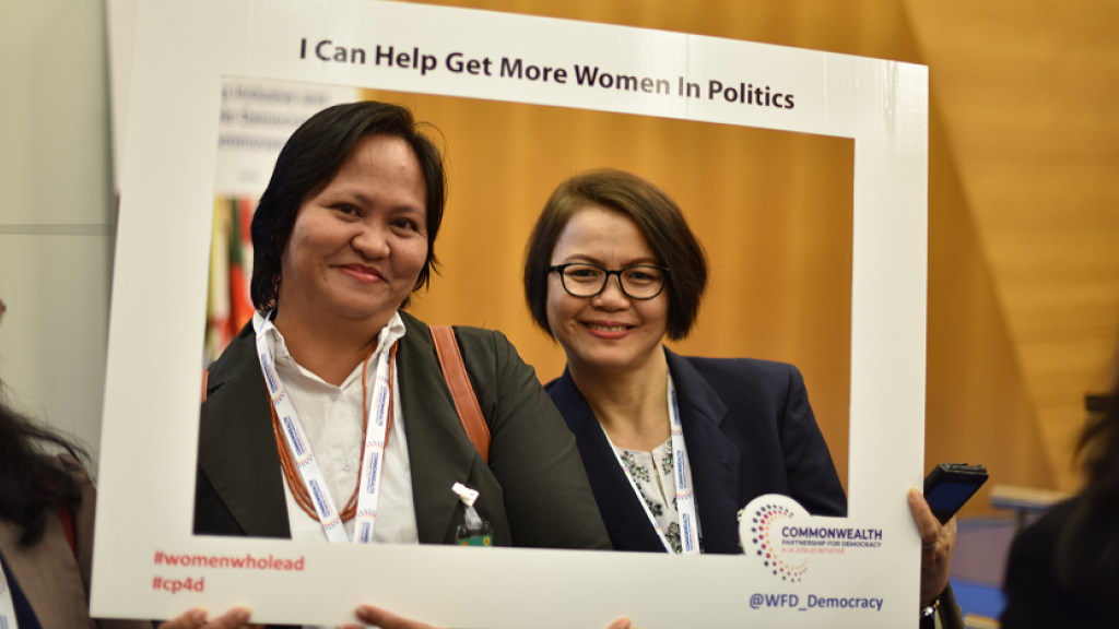 Two people holding up a sign that says I can help get more women in politics