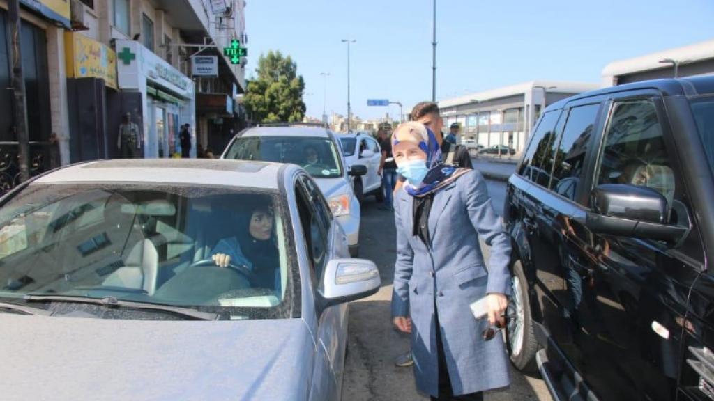  A woman standing talking to another in a car