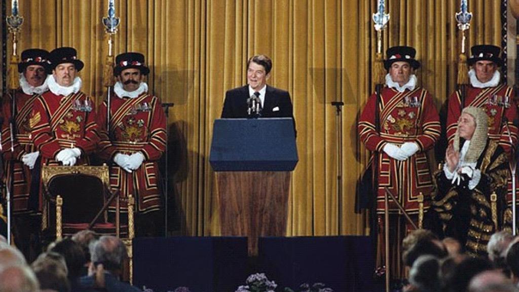 Ronald Reagan standing at a podium between Palace of Westminster officials delivering his speech