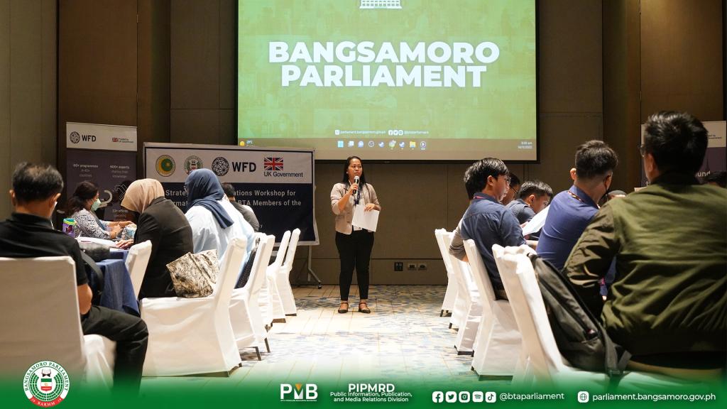 A woman with a microphone stands in front of an audience. Behind her a screen says Bangsamoro Parliament