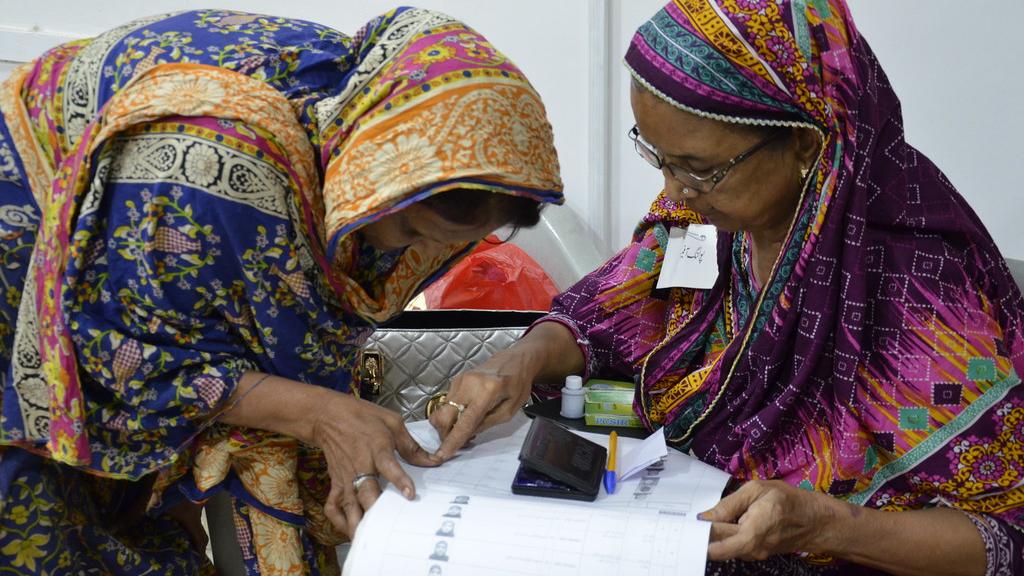 A polling official confirms a voter's identity during the Pakistani general elections in July 2018. The two women are wearing colourful clothing and headscarves