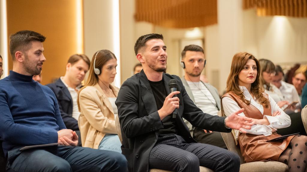 A person speaking using a mic while sitting around others