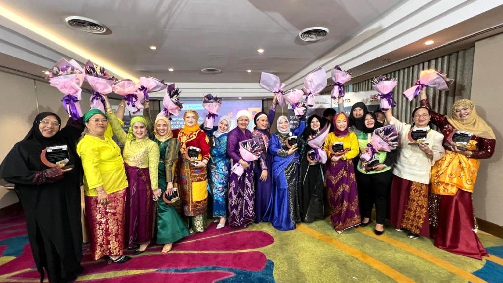 A group of women smiling and holding bunches of flowers in the air