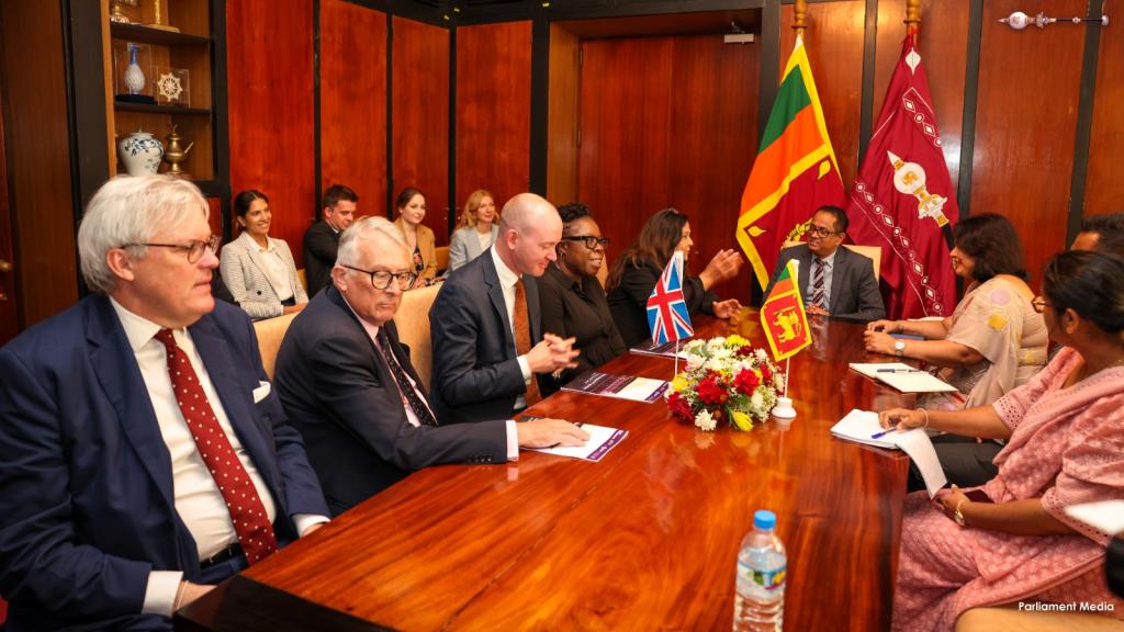 Parliamentary delegation consisting of a group of men and women are in discussion. Sri Lanka and UK flags can be seen in the photo. 
