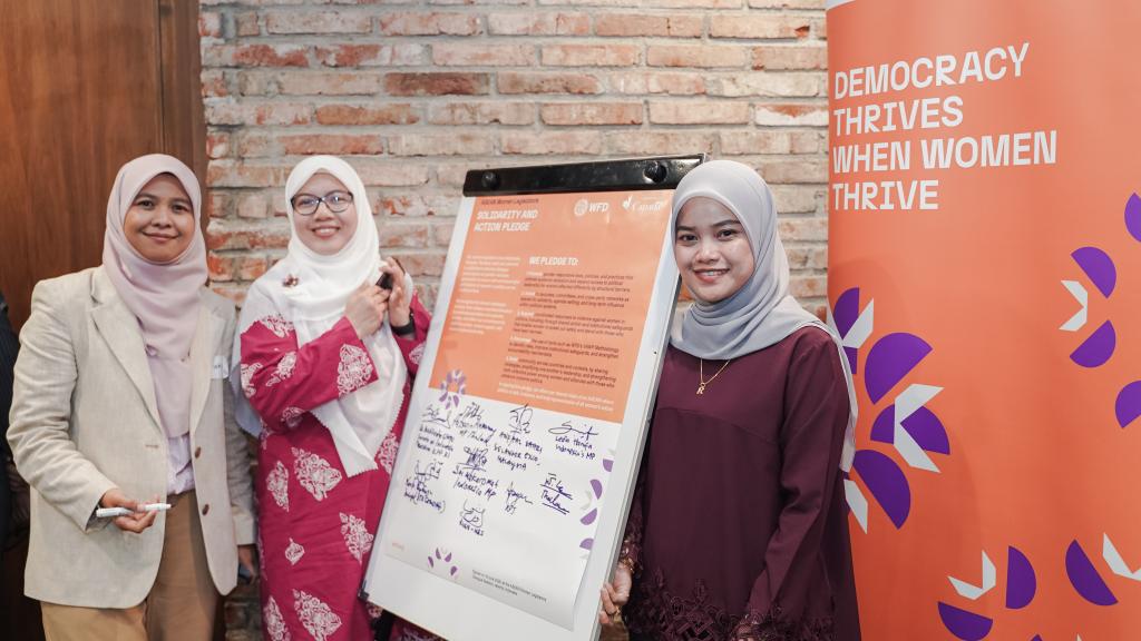 Three women standing next to a white board that shows signatures.