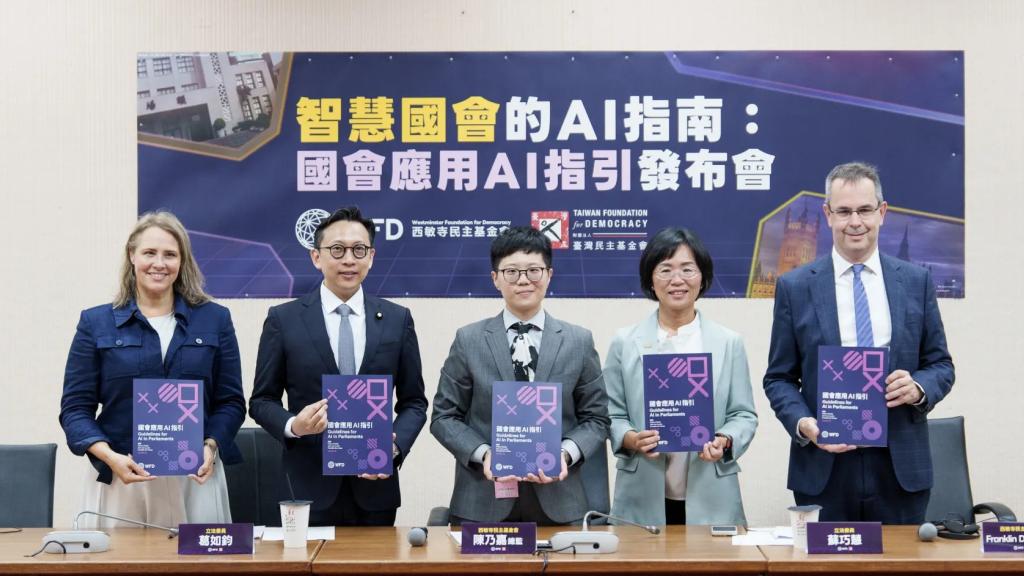 Three women and two men stand in front a table. Each of them holds a book in front of them. 