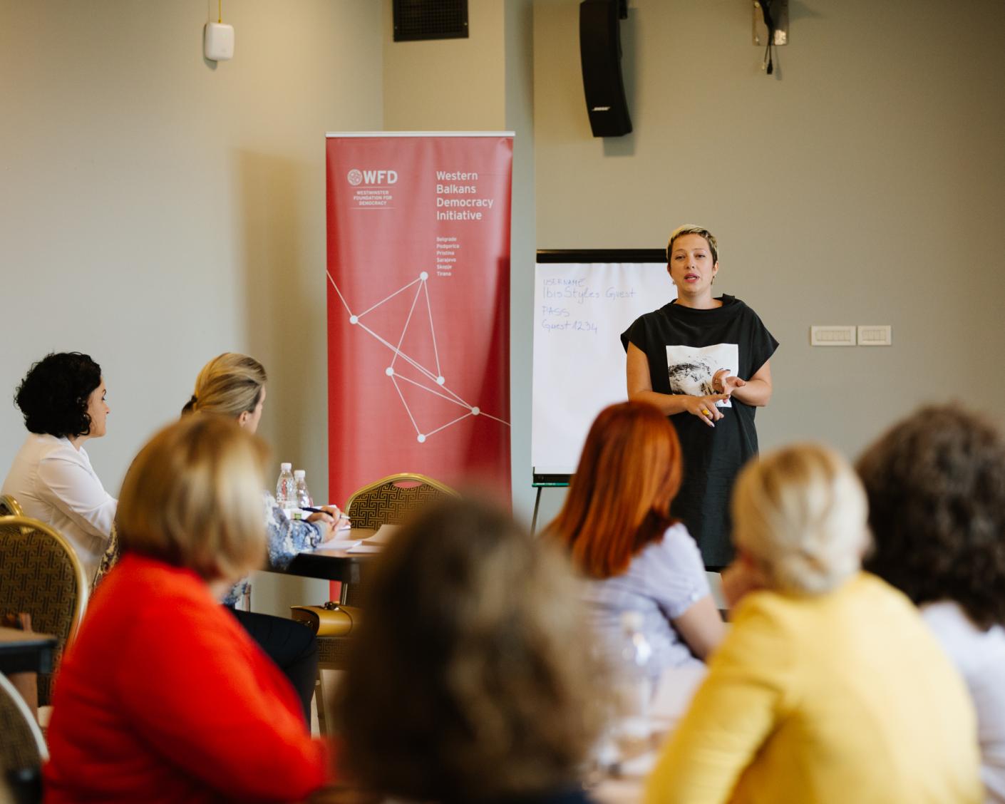 a woman giving a presentation next to a WBDI banner