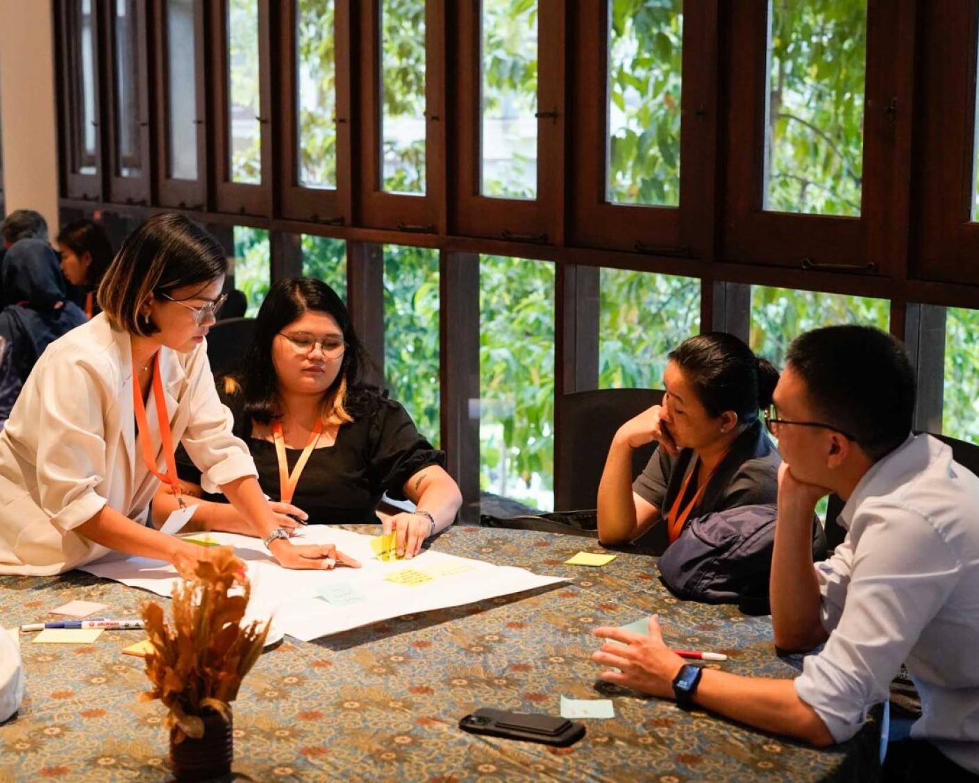 A group of 4 people are discussing around a plain piece of paper which they are sticking post-its to