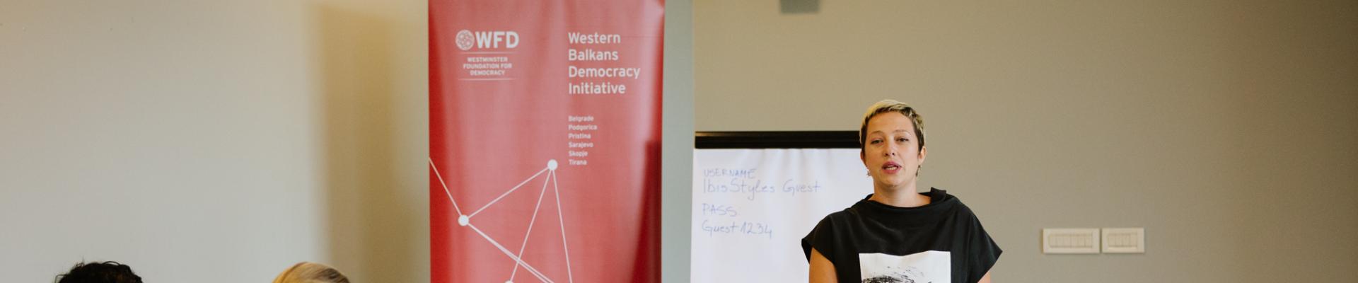 a woman giving a presentation next to a WBDI banner