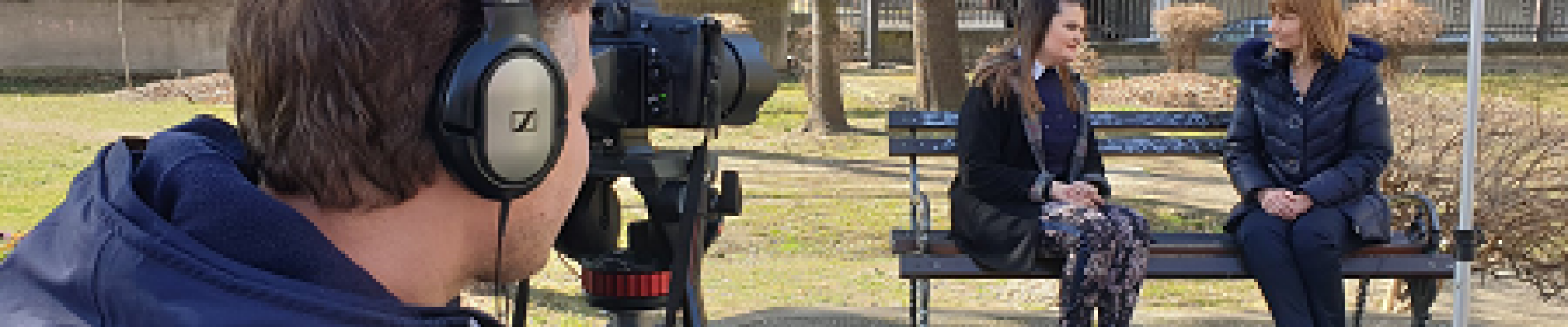 A person filming two people sitting on a bench