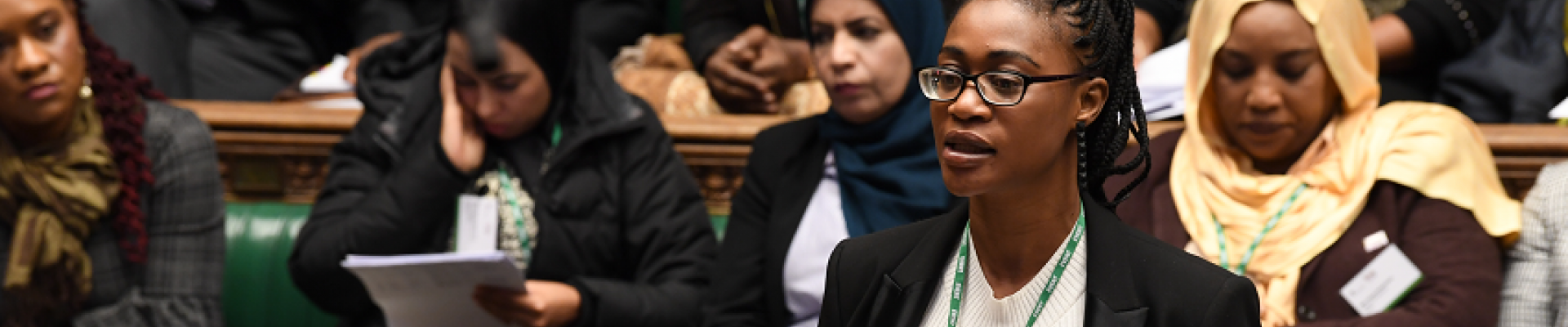 A woman speaking in the midst of other sitting women in the UK Parliament