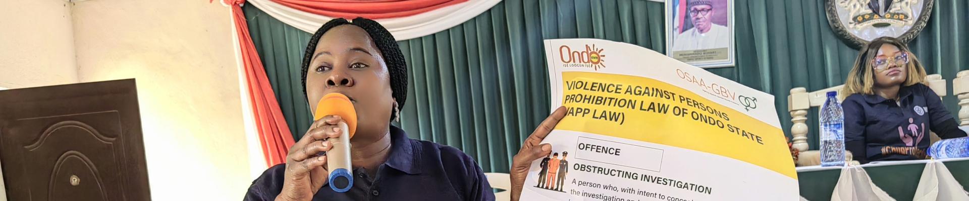 A woman holding an advocacy paper while speaking on a microphone