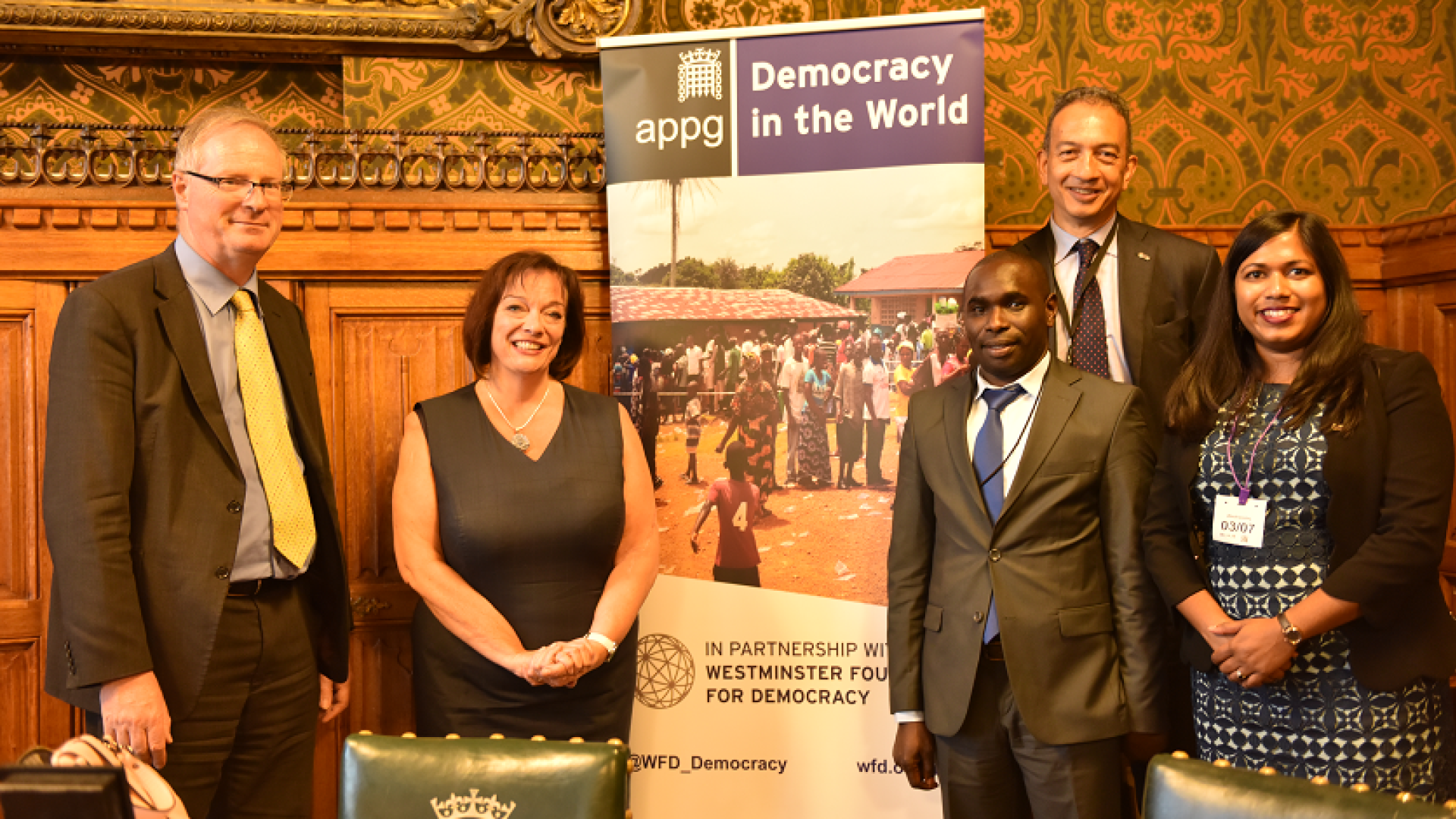 two ladies and three men posing by a banner