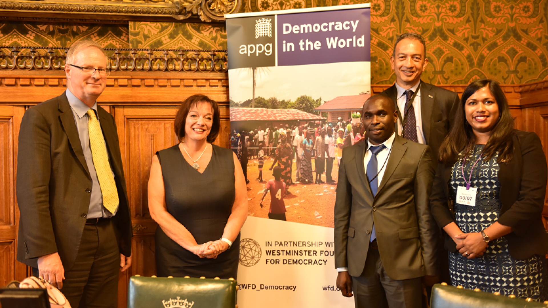 two ladies and three men posing by a banner 