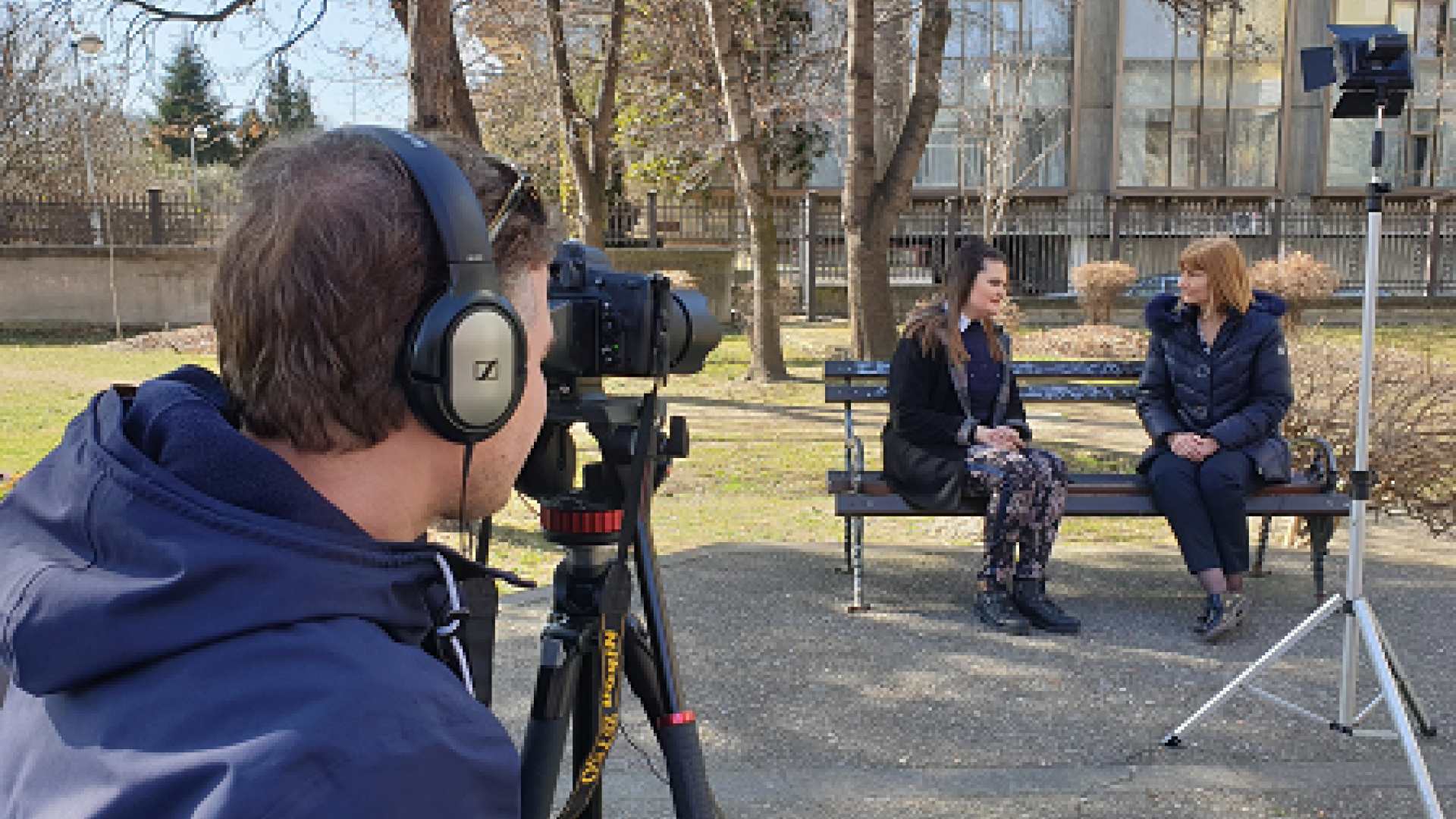 A person filming two people sitting on a bench