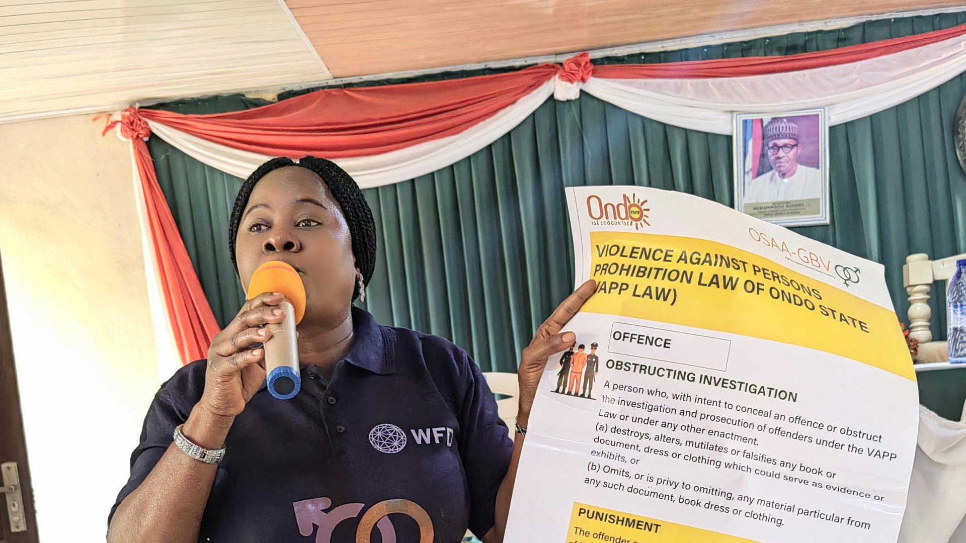 A woman holding an advocacy paper while speaking on a microphone