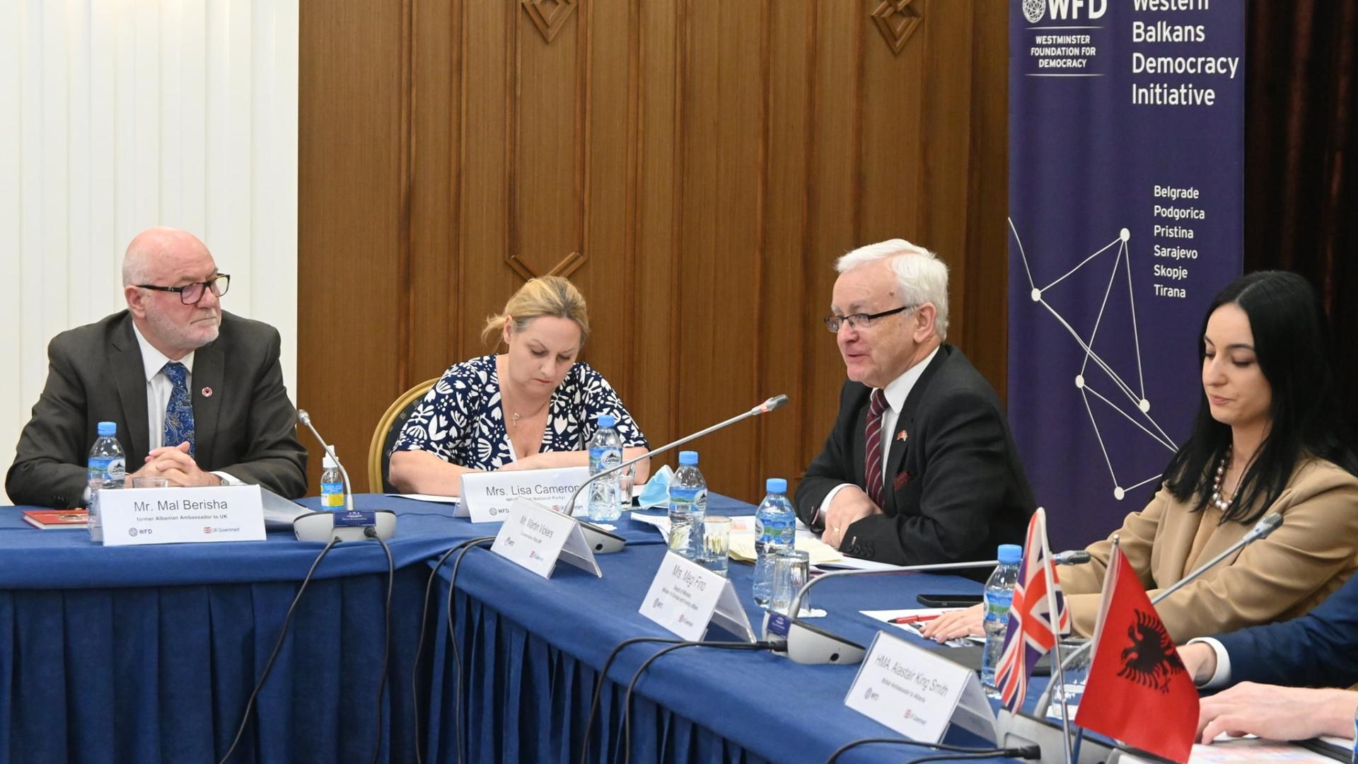 A panel of people sitting at a table. One is speaking into a microphone.