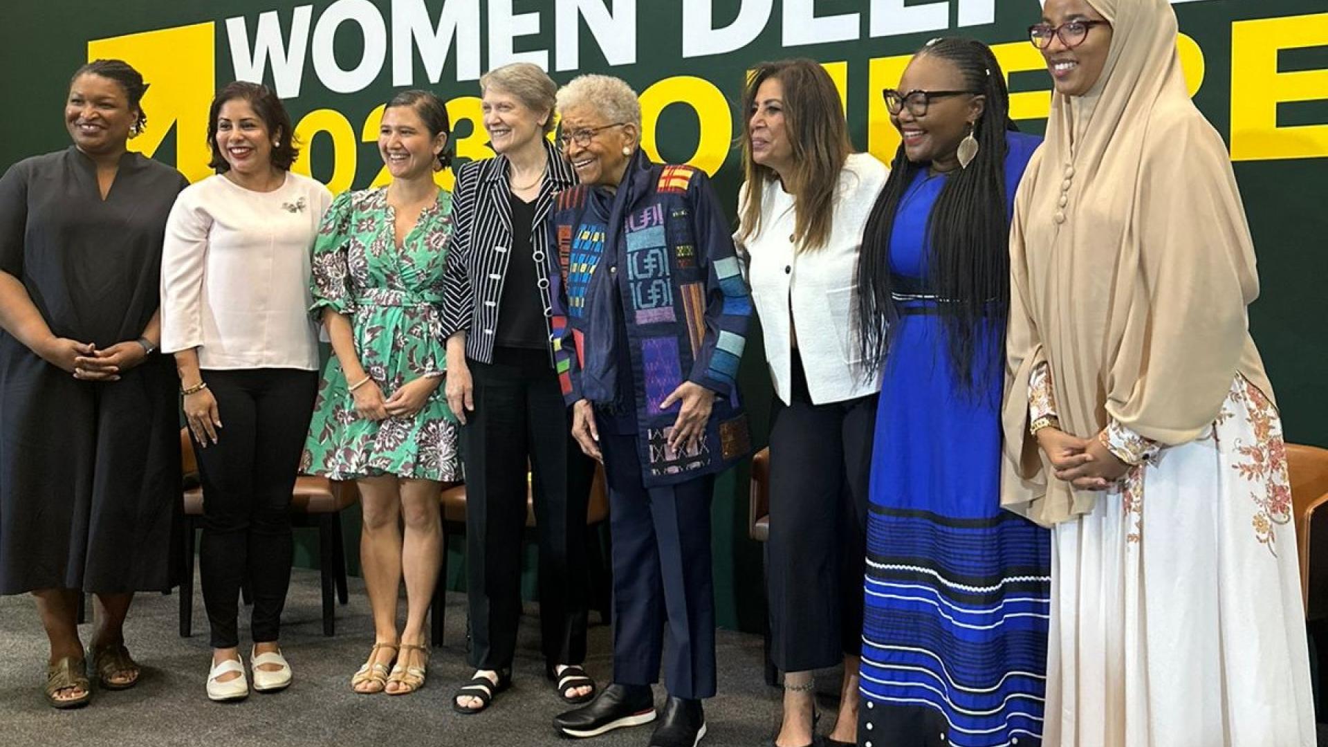 A line of woman in front of a billboard that says women deliver conference