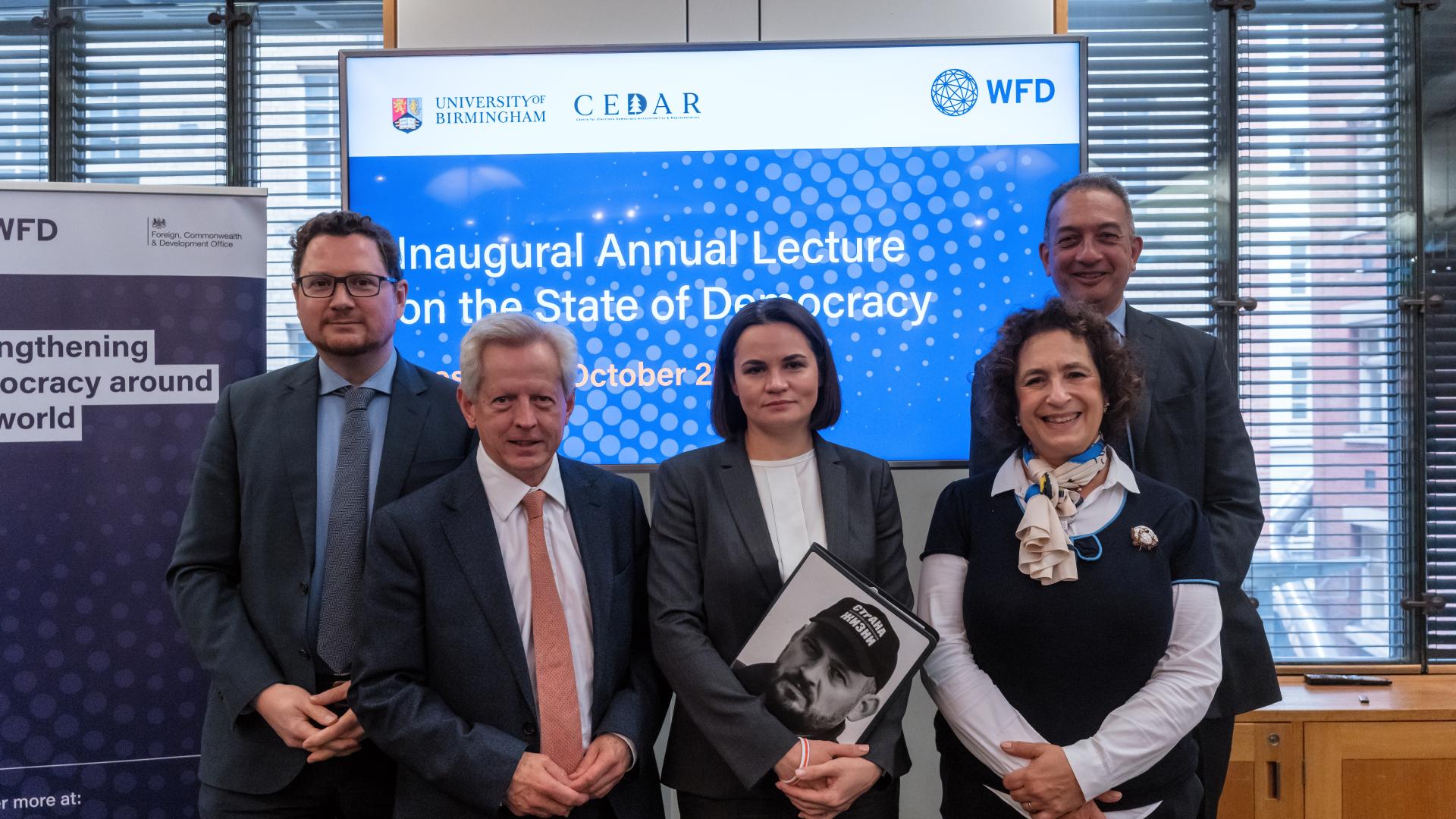 Two women and three men stand in front of a screen that says Inaugural Annual Lecture on the State of Democracy