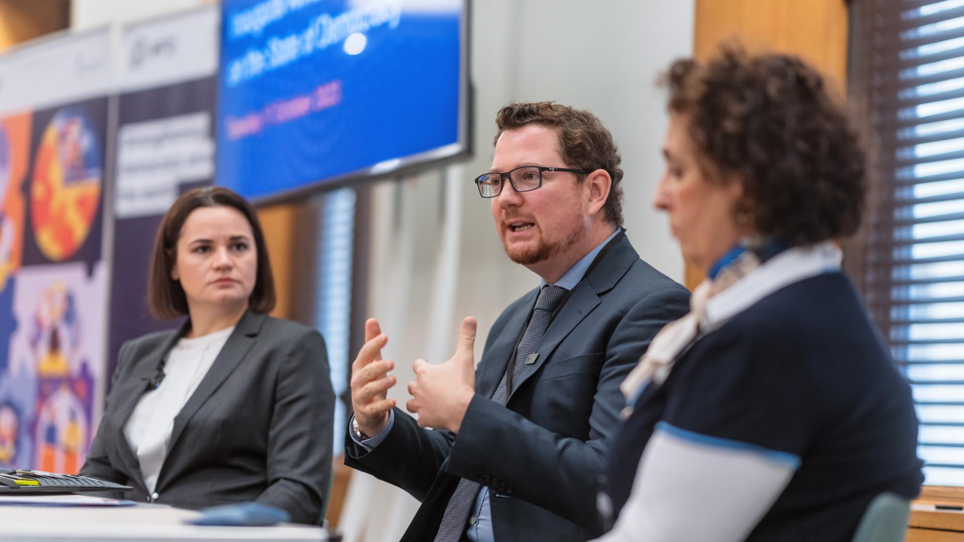 A man sits between two women. He is gesticulating