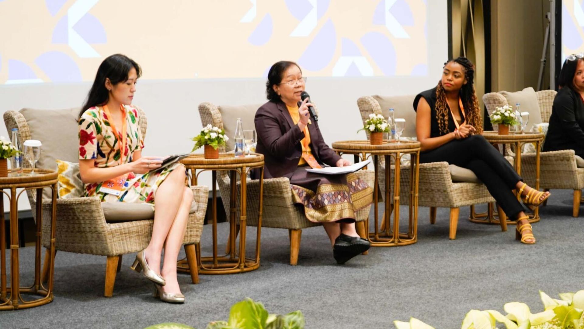 Three women seated on a panel. The woman in the centre speaks into a microphone