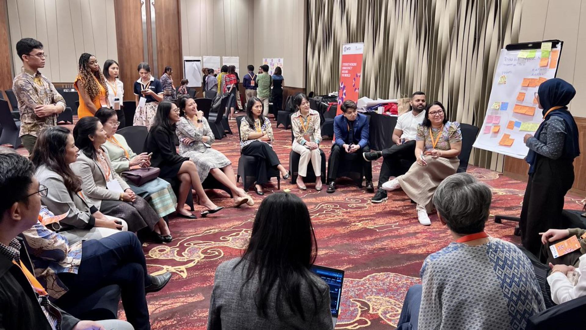 A group of people sit in a circle looking at a flipchart