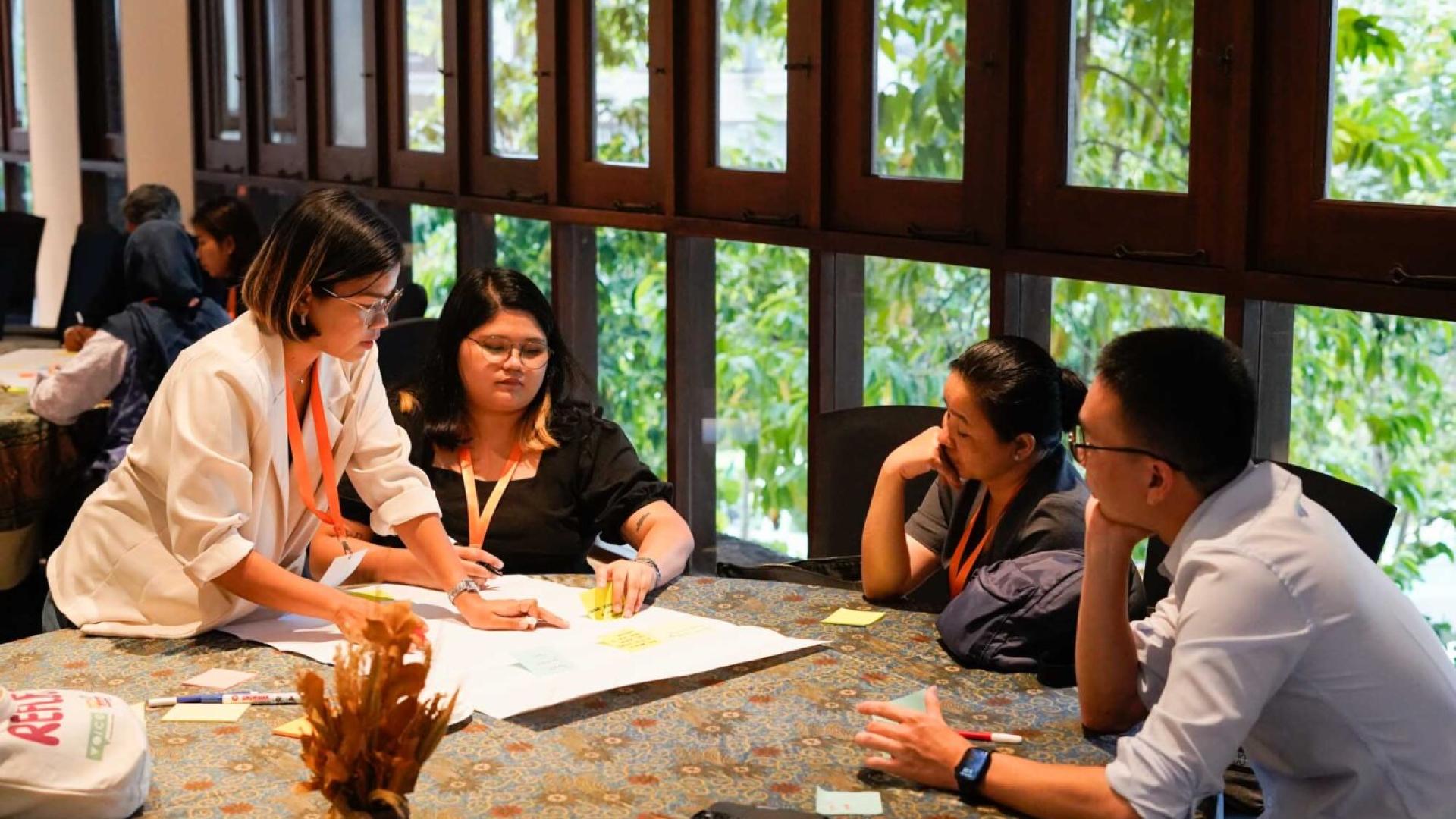 A group of 4 people are discussing around a plain piece of paper which they are sticking post-its to