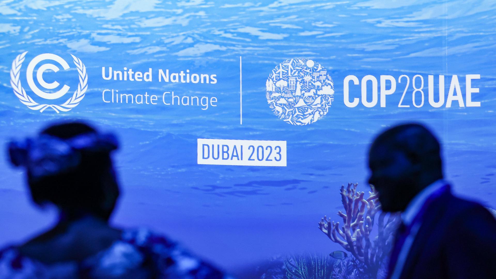The COP28 logo on a blue sea background with the figures of two people in front