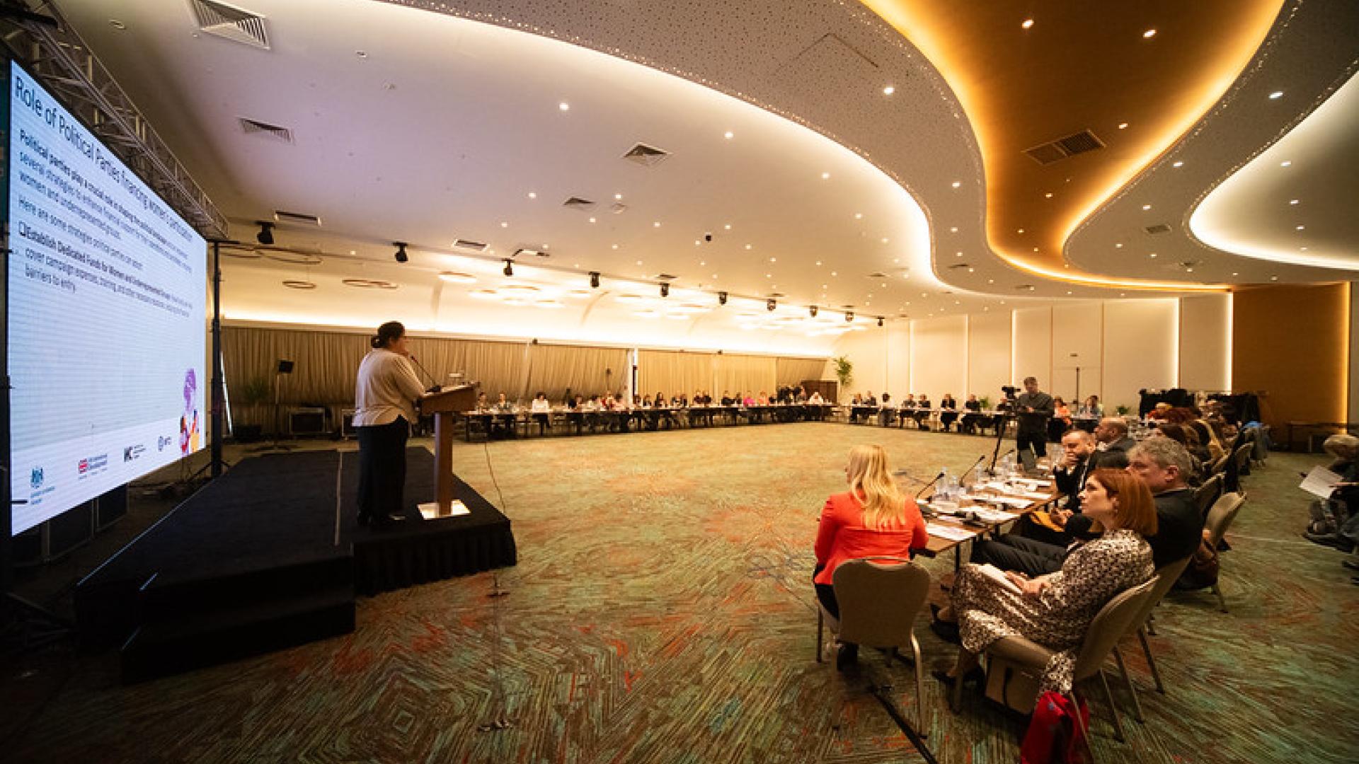 A group of people sit around the edges of a large conference room