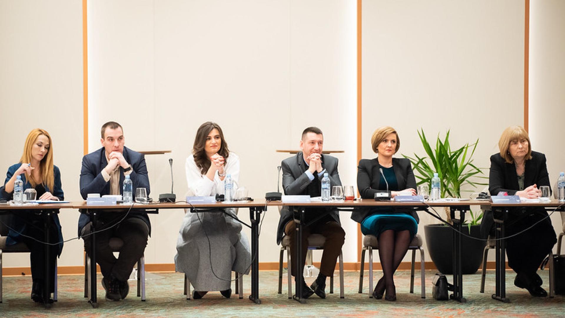 Five people speaking on a panel sit behind a table listening attentively