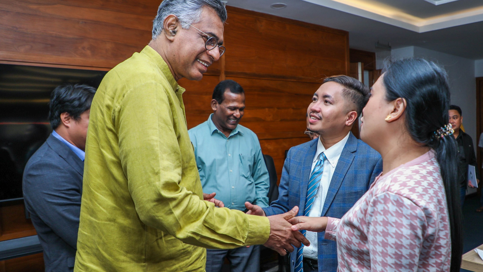 A group of people with two in the foreground shaking hands.