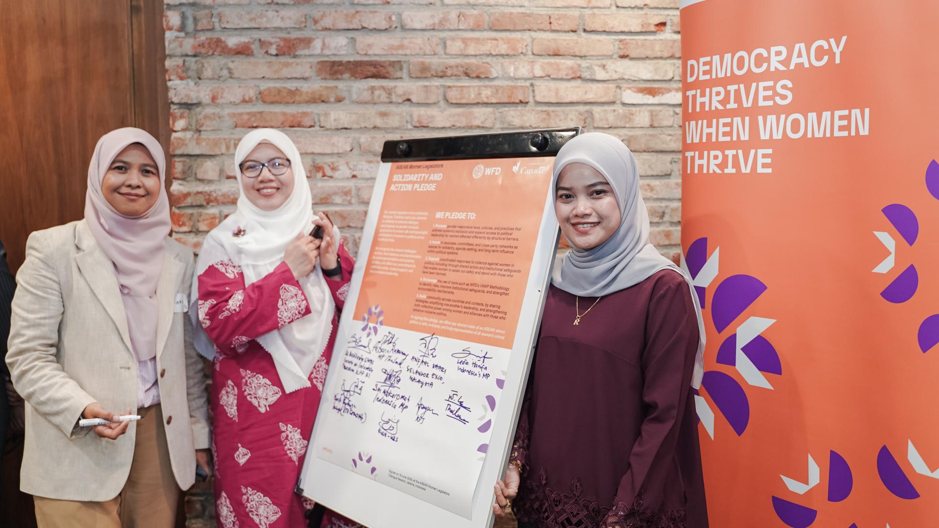 Three women standing next to a white board that shows signatures.