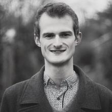 a man smiling at the camera wearing a coat and a shirt