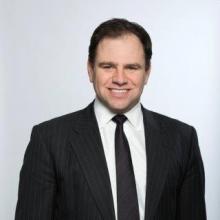 A white man in a suit and tie smiling at the camera